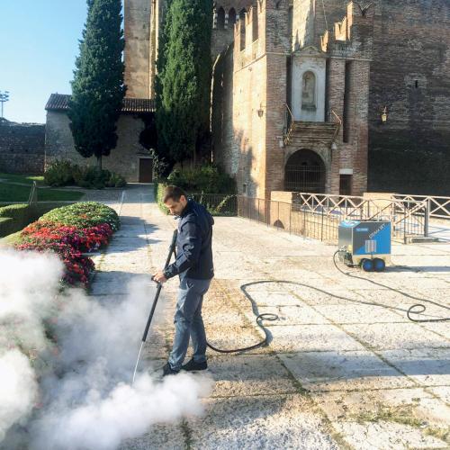 Commercial weed steamer in action, demonstrating eco-friendly weed control in a landscaped area near a historic building. This steam weed control method is ideal for maintaining cleanliness and safety in public and commercial spaces without using chemicals.