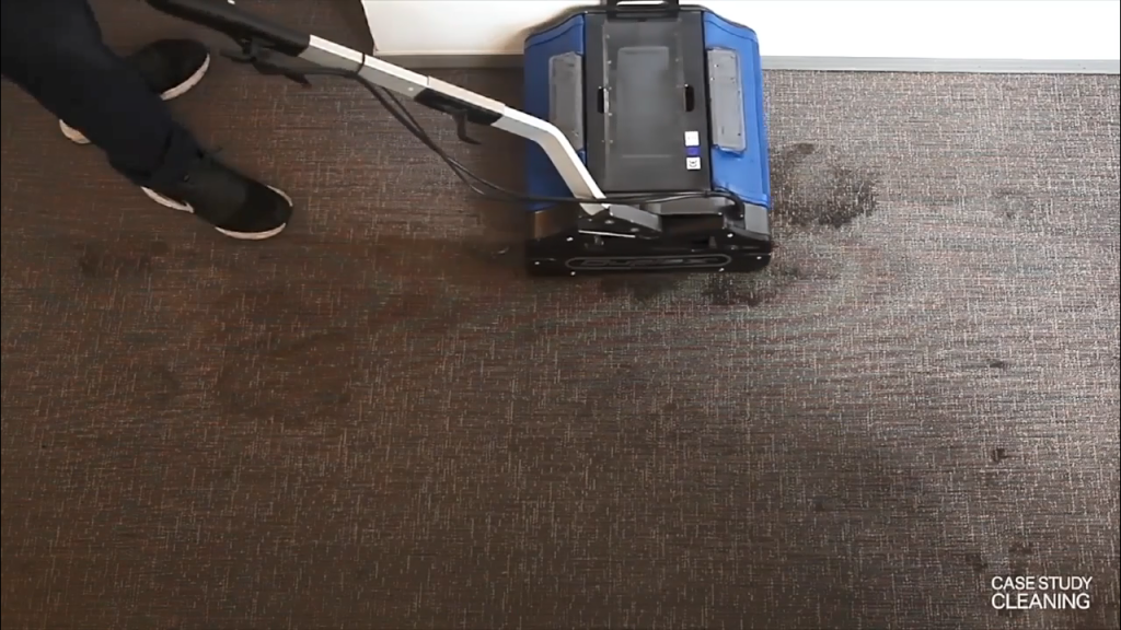 Duplex carpet machine removing stains from a wet patch on dark commercial carpet.