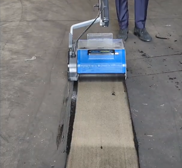 Duplex cleaning machine removing heavy dirt from a concrete floor in an industrial setting.