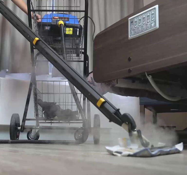 Jetsteam Maxi commercial steam cleaner connected with a steam mop, cleaning a healthcare facility floor with visible steam and medical equipment in the background.